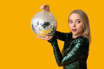 Beautiful young woman with disco ball on yellow background