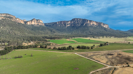 Drone aerial photograph of lush agricultural farmland and vegetation along the cliff face in Capertee Valley in Wollemi National Park in the Central Tablelands of NSW, Australia.