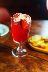 A beautiful strawberry cocktail with whipped cream on a wooden table.