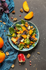 Plate of delicious salad with persimmon, pomegranate seeds and walnut on black background