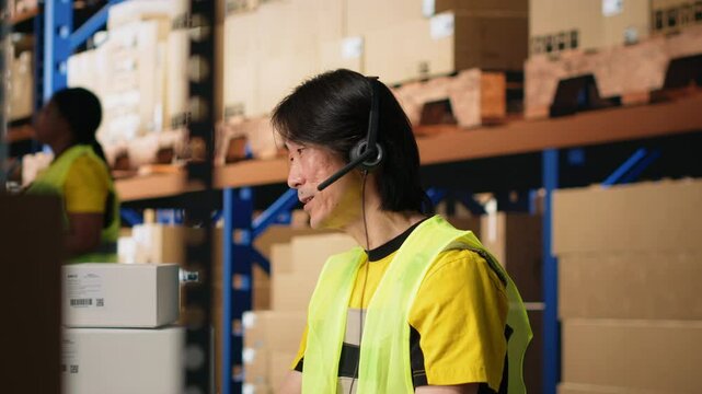Call center male worker answer help line calls in a logistics warehouse, updating clients on orders and resolving cargo mix ups. Managing shipping software and airway bills. Camera B.
