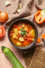 Black bowl with delicious beef stew and ingredients on pink tile background