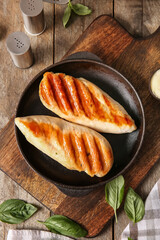 Frying pan with tasty grilled chicken breast and basil on wooden background