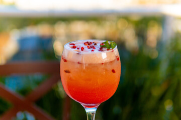 Elegant cocktail with a gradient of red and orange hues, garnished with berries and mint.