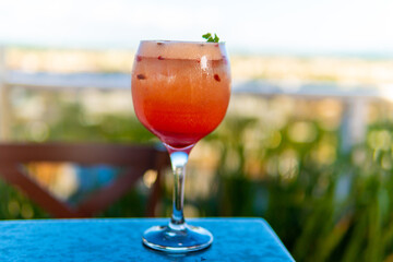 A colorful cocktail in a stem glass is set on a blue table with a beautiful background.