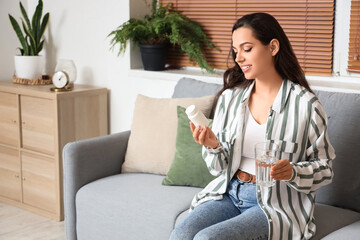 Young woman with glass of water reading pills description at home