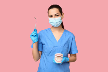 Portrait of female dentist in mask with jaw model and dental mirror on pink background