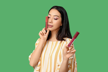 Fototapeta premium Beautiful Asian woman with different lipsticks on green background
