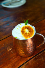 A beautifully crafted cocktail with whipped cream and an orange slice in a copper mug.