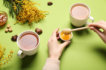 Young woman adding honey into tea on green background