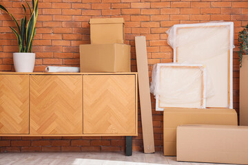 Furniture, houseplant and cardboard boxes with belongings near brown brick wall. Moving house...
