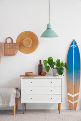 Stylish interior of modern hall with chest of drawers and surfboard