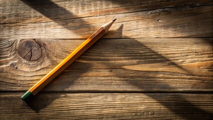 A pencil lies on a worn wooden desk with a faint shadow of an unfinished sketch