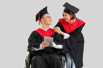 Male graduate in wheelchair with his classmate using tablet computer on light background