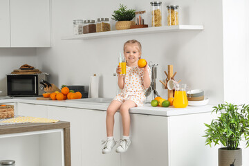Cute little girl with glass of orange juice and citrus fruits in kitchen