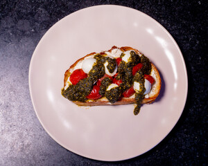 Bruschetta with pesto, tomatoes, and mozzarella cheese on a plate, ready to eat.