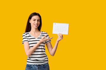 Beautiful young happy woman pointing at calendar on yellow background