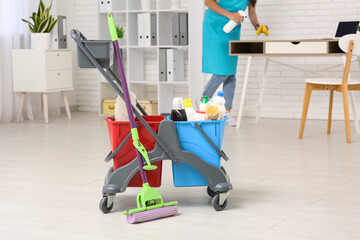 Female janitor with trolley and cleaning supplies cleaning office