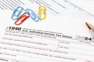A U.S. tax document Form 1040 is placed neatly on a desk alongside a pen, representing the annual...