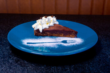 Delicious slice of chocolate cake with whipped cream served beautifully on a blue plate.