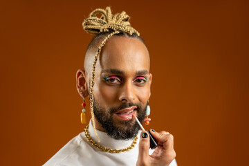 African american gay applying make up lipstick isolated on orange. Handsome guy wear bright make-up apply lips with lipstick. Fashion lgbtq concept. Male makeup artist close up portrait