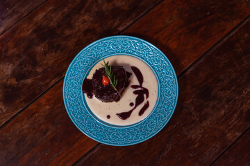 Delicious steak with rich sauce on a teal plate, served on a wooden table.