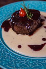 Delicious gourmet steak dish, perfectly cooked and beautifully presented on a teal plate with an artistic sauce design.
