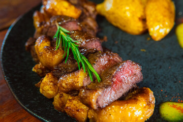 Delicious steak slices with roasted potatoes and fresh rosemary on a dark plate.