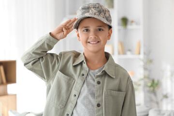 Cute little boy in military cap saluting at home. Veterans Day celebration