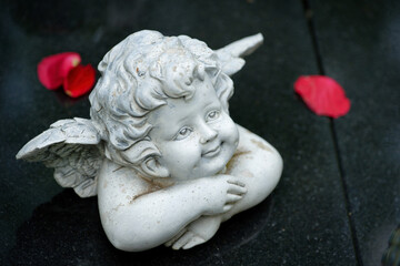 a small cherub on a dark gravestone looks up with a gentle smile surrounded by a few bright red...