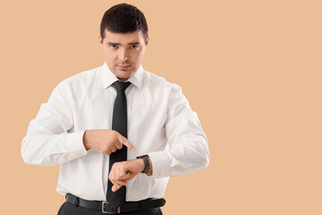 Young businessman pointing at wristwatch on beige background. Time management concept