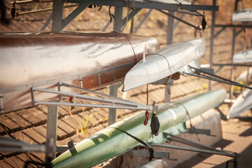 Shallow depth view of stacked racing shells on boathouse rack, metallic and fiberglass hulls for...