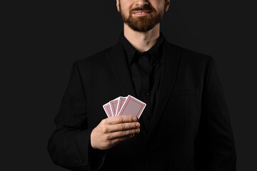 Handsome young man with playing cards for poker on black background, closeup