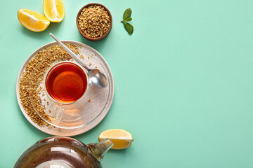 Glass cup and teapot of hot buckwheat tea with lemon on turquoise background