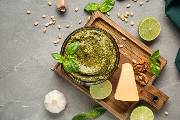 Wooden board with bowl of delicious pesto sauce and ingredients on grey grunge background
