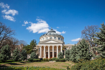 Ateneul Roman main facade in front of a park during a sunny afternoon. with the mention Ateneul Roman meaning in Romanian Athenaeum. It is a concert hall and venue, a major landmark of Bucharest.