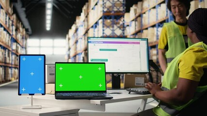Multiethnic team of warehouse workers next to green screen monitor. Managing shipping labels, barcode scanner data or e-commerce inventory tracking systems in industrial warehouse. Camera A. - Powered by Adobe
