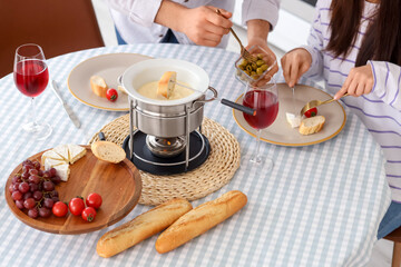 Young couple eating snacks with cheese fondue and glasses of wine at home, closeup