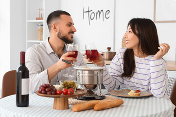 Young happy couple with glasses of wine, snacks and cheese fondue at home
