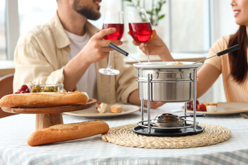 Young couple with snacks and cheese fondue drinking wine at home, closeup