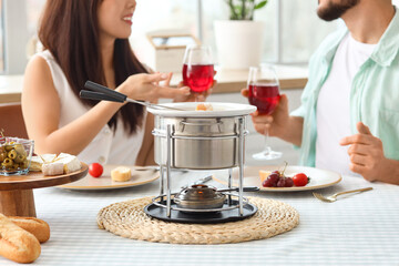 Young couple with snacks and cheese fondue drinking wine at home, closeup