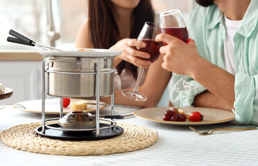 Young couple with snacks and cheese fondue drinking wine at home, closeup