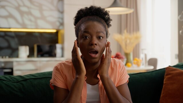 Shocked amazed excited African American ethnic woman female girl lady homeowner businesswoman client customer looking at camera open mouth wow surprised delight emotions indoors living room apartment