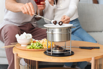 Young couple with glasses of wine dipping marshmallows into chocolate fondue at home, closeup
