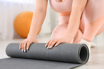 Sporty plus size woman rolling out fitness mat at gym, closeup