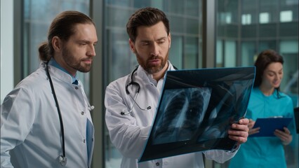 Thoughtful confused two Caucasian men males doctors radiologist and physician holding lungs scan...