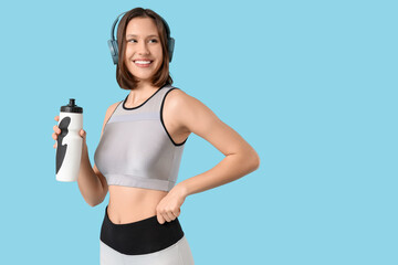Sporty young woman in headphones with water bottle on blue background