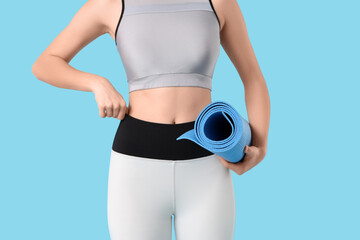 Sporty young woman with fitness mat on blue background