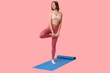 Sporty young woman training on mat against pink background