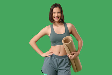 Sporty young woman with fitness mat on green background